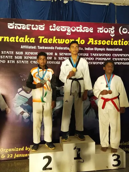 A student stands at the top of the podium, number one. This is from the Karnataka Taekwondo Association state championship. We aim for the gold.