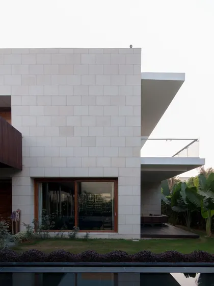 The exterior combines clean lines of modernism with the texture of natural stone cladding. Deep overhangs provide shade and create sheltered outdoor seating areas, blurring the line between the built form and the garden.