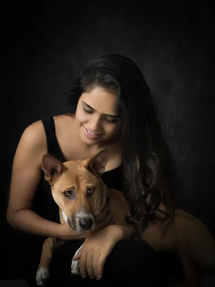 A classic, dramatic studio portrait of a woman and her indie dog against a dark background. The lighting beautifully highlights their features and the quiet bond between them.
