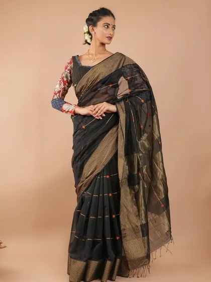 A sophisticated black Maheshwari silk cotton saree with a gold border and subtle woven details. It’s paired here with a printed blouse for a touch of artistic flair.