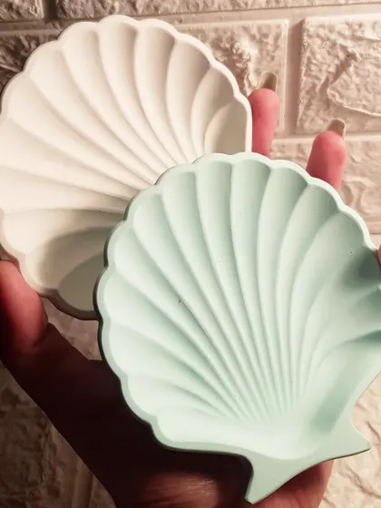 A pair of mini shell dishes in our hands, one in white and one in a soft mint green.