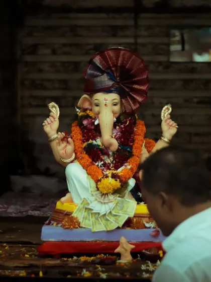 An intimate and poignant moment of a devotee offering prayers to a Ganesh idol before the visarjan. The dark, moody lighting and the focus on the personal act of worship create a powerful feeling of devotion.