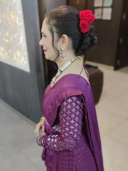 A side profile showcasing an elegant hair bun adorned with red roses. This hairstyle is paired with subtle makeup, making it a perfect look for a sophisticated evening party.