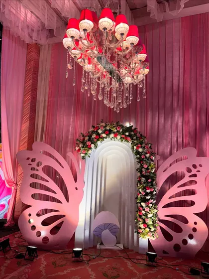 This elegant photo backdrop for a baby welcome features large butterfly wings, a floral arch, and a beautiful chandelier.