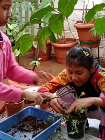 Two children work together to pot a plant, sharing the task and learning through collaboration.