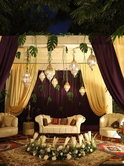 A cozy and elegant seating area for a reception, with Moroccan-style lanterns, plush sofas, and rich purple and gold drapes.
