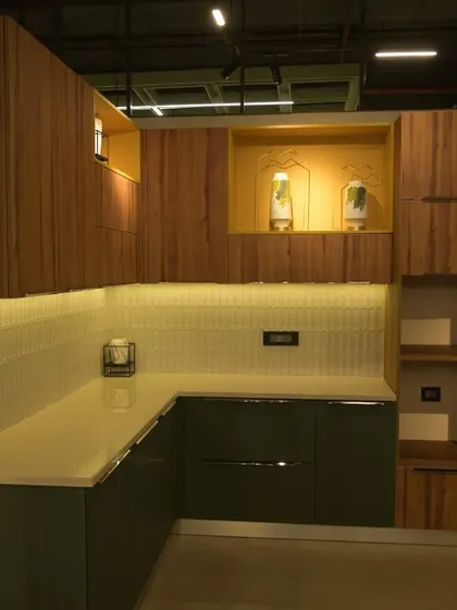 A kitchen display at my Kolkata Experience Centre, showing a combination of wood-finish and dark green cabinets, a tiled backsplash, and an integrated marble puja unit.