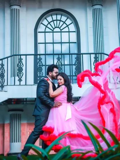 A romantic pre-wedding photo of a couple in a pink gown and dark suit, set against a grand white building, perfect for a classic and elegant theme.