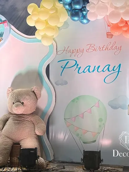 A grand stage setup for a first birthday, with a large teddy bear prop, marquee '1', and a custom backdrop.