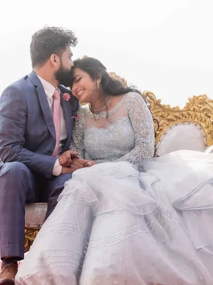 A medium shot of the couple on their engagement sofa. The groom's gentle kiss on the bride's head captures a perfect, loving moment.