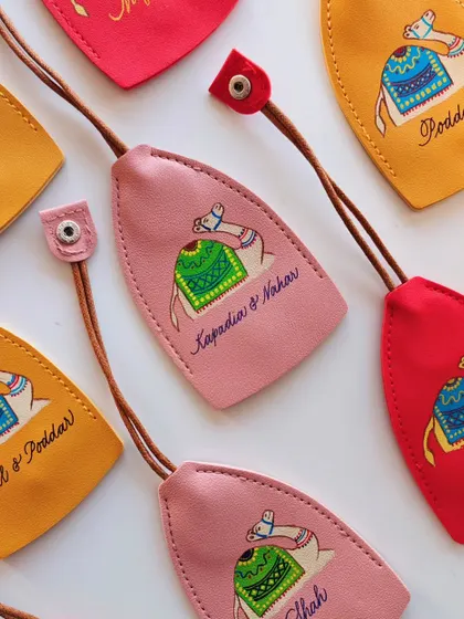 An array of colorful, hand painted leather keychains, each personalized for different families like 'Kapadia & Nahar' and 'Mittal & Poddar'. These make for wonderful, bespoke wedding or event favors.