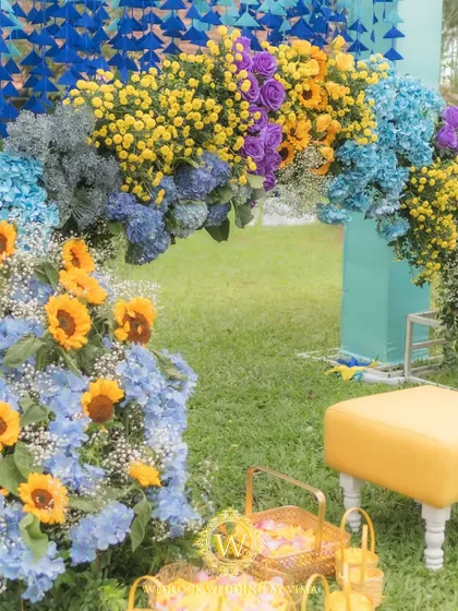 A vibrant floral backdrop and welcome sign for a colorful Haldi and Mehendi ceremony. The mix of orange, blue, purple, and yellow flowers created a stunning photo opportunity for the couple and their guests.