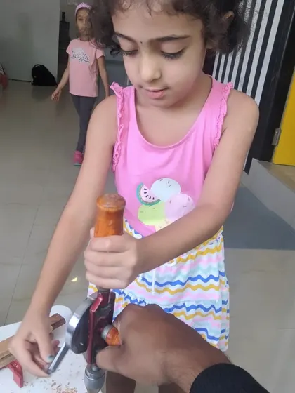 An instructor's hands guide a young girl as she gets the feel for using a hand drill for the first time.