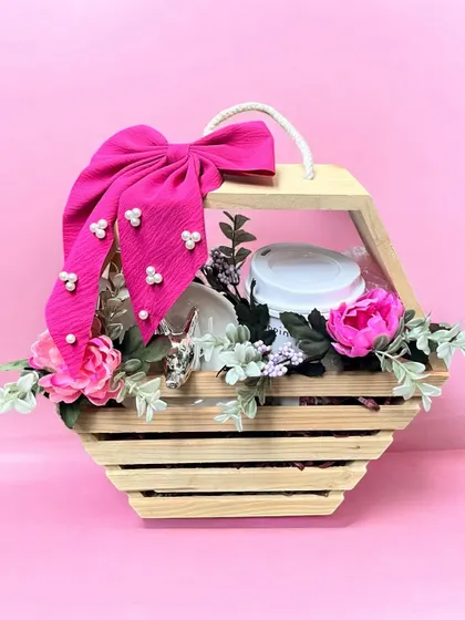 This rustic yet chic hamper is presented in a hexagonal wooden basket. Adorned with a large pink bow and faux flowers, it's a beautiful way to gift a collection of curated items.