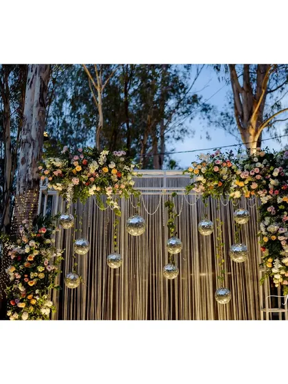 The Sangeet stage is a beautiful combination of a thread backdrop, disco balls, and floral arrangements, creating a unique and artistic setting.