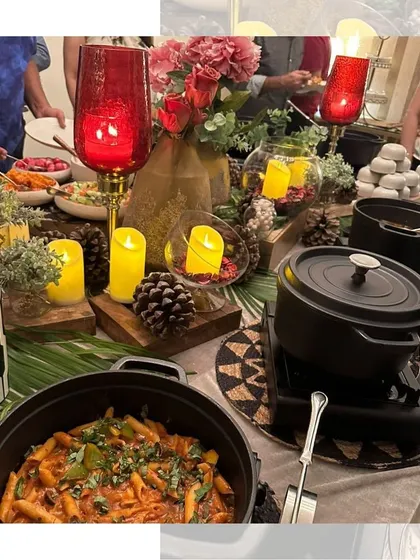 A warm and inviting Diwali buffet table, decorated with red lanterns, candles, and pinecones, featuring a delicious spread of pasta and other dishes.