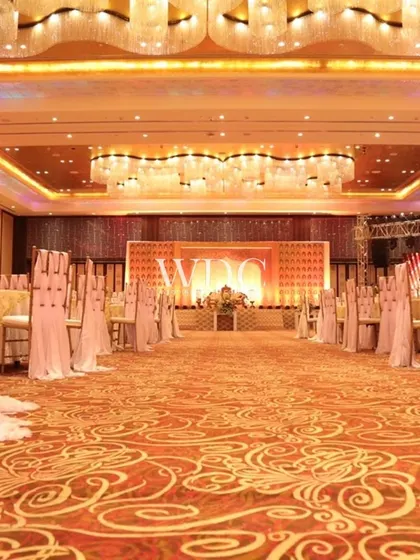 A view of the grand ballroom at the Taj, set up for a wedding. The long aisle is flanked by elegantly draped chairs, leading to a magnificent stage, all under the glow of grand chandeliers.