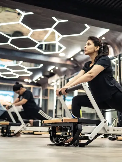 Clients perform a lunge on the Reformer, a great exercise for toning the legs and glutes. The modern studio with its unique ceiling design provides an inspiring backdrop for the workout.