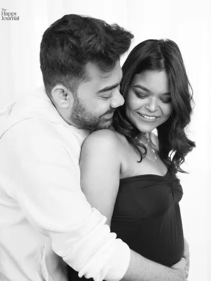 A black and white portrait that emphasizes the emotional connection. The husband's embrace from behind is a classic pose that speaks of love and protection.