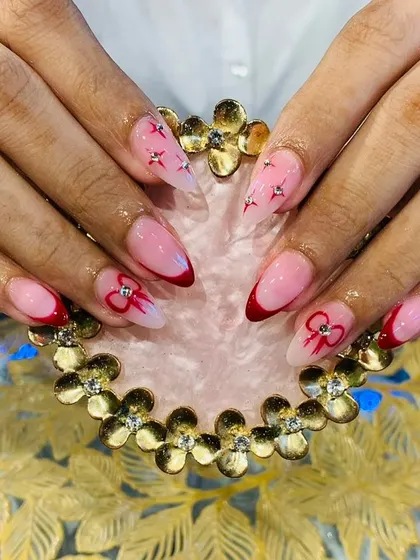 A creative take on the French manicure with red tips, bow designs, and star-shaped rhinestone accents.