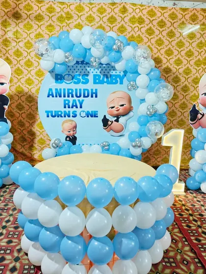 A Boss Baby first birthday setup with a balloon-wrapped table. This decoration is perfect for a cake-cutting ceremony, featuring character cutouts and a light-up number '1'.
