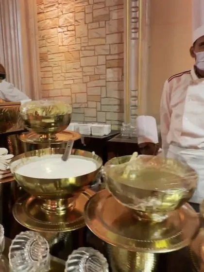 A chef stands proudly behind a live station featuring various accompaniments and chutneys served in traditional brass bowls, ready to customize dishes for guests.