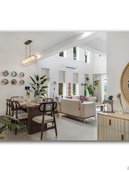 An open-plan living and dining area in Goa, filled with natural light and greenery. The space feels bright and connected, with a clear view from the dining table through to the living room and the lush outdoors.