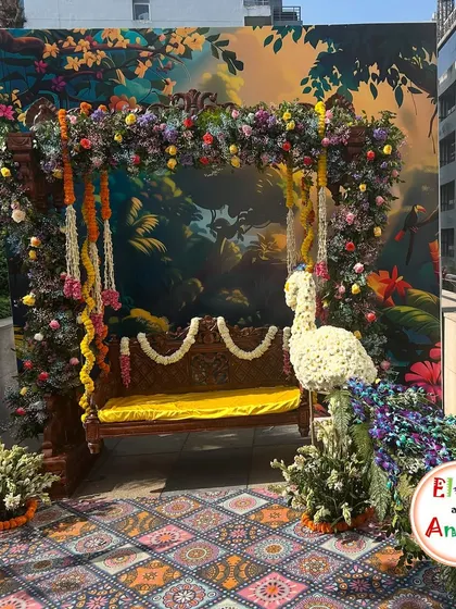 For a Mehendi ceremony with a traditional theme, I designed this stunning seating area. A classic wooden swing, or jhoola, is framed by a lush arch of fresh flowers and garlands. The centerpiece is a custom peacock crafted entirely from white flowers, set against a vibrant, artistic backdrop to create a picturesque spot for the bride.