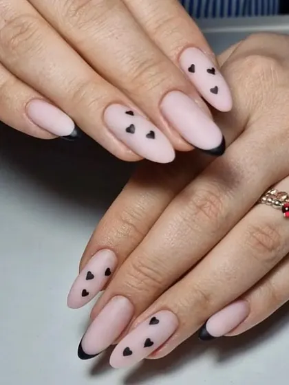 A chic and edgy look, these matte nude almond nails are decorated with tiny black hearts and a sharp black French tip.