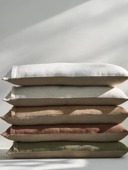 A stack of linen cushions in earthy, neutral tones. The clean, simple composition and natural lighting make this a versatile and attractive shot for any home decor brand.