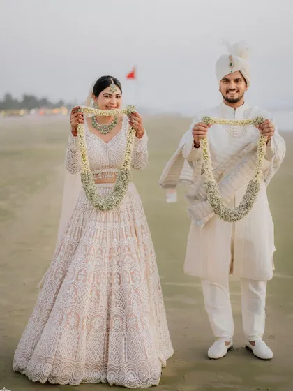 A playful shot of the couple on the beach, holding up their varmalas for the camera.