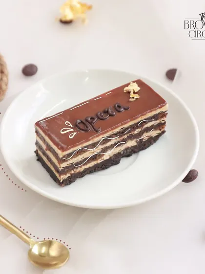 A tribute to French patisserie, our Coffee Opera cake features layers of almond sponge soaked in coffee syrup, coffee buttercream, and chocolate ganache.