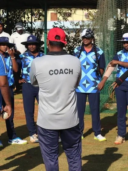 A coach addresses the women's team in a huddle, discussing strategy and motivating the players before a crucial match.