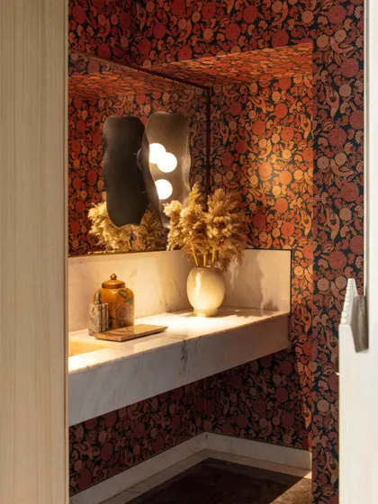 The powder room is a jewel box of opulence, featuring a luxurious Sabyasachi wallpaper. A stunning wall sconce by Shailesh Rajput and wooden fluted paneling create a warm, intimate, and sophisticated atmosphere.