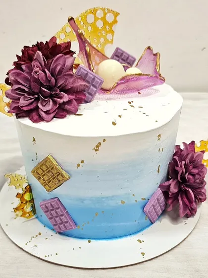 This watercolor buttercream cake is decorated with chocolate sails, chocolate bars, and fresh flowers. Students learn how to blend colors smoothly on the cake's surface for a beautiful gradient effect.