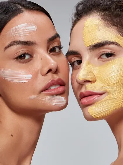 A comparative beauty shot featuring two models using different face masks. This image effectively showcases product variety within a single frame, demonstrating a white cream mask and a yellow clay mask for a skincare brand.