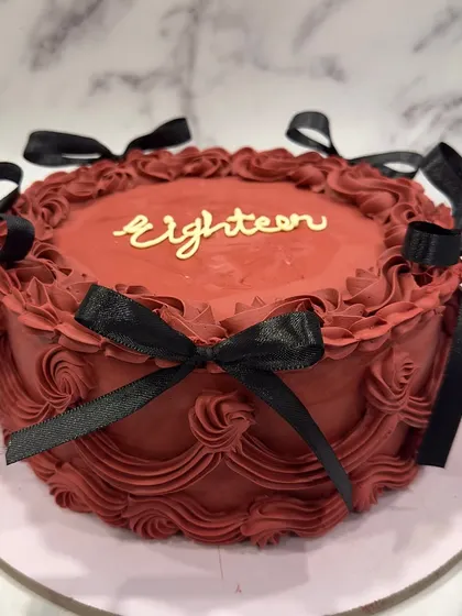 A bold and dramatic vintage-style cake for an 18th birthday. The deep red buttercream is decorated with intricate piping and finished with contrasting black satin bows.