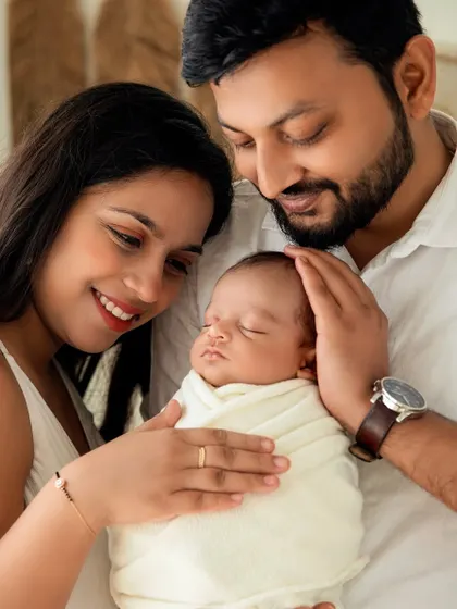 A close-up of the family, showing their gentle hands on their sleeping baby. A portrait of unity and love.