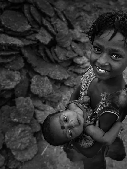 The same portrait of the smiling girl and baby, presented in black and white. The monochrome version emphasizes the emotional connection and the textures of their surroundings.