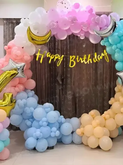 A whimsical pastel-colored circular balloon arch for a birthday. The arch is decorated with moon and star foil balloons and a large number '1' balloon pillar.