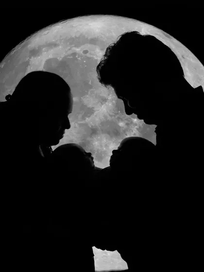 A beautiful silhouette portrait of a family with their twin newborns against the moon.