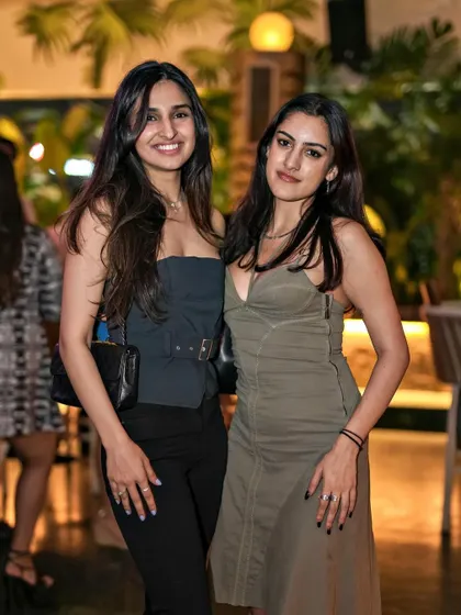 Two friends in stylish olive and black outfits, posing against the lush backdrop of Pangeo.