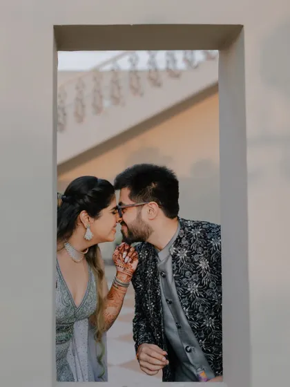 A sweet, stolen moment framed by a window, capturing the intimacy and romance of the couple.