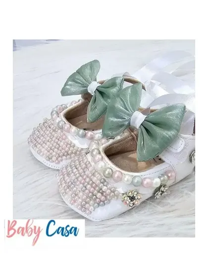 Step into comfort and style with these adorable, handcrafted baby shoes. These white bellies are adorned with pearls and a sweet green bow, perfect for a little princess.