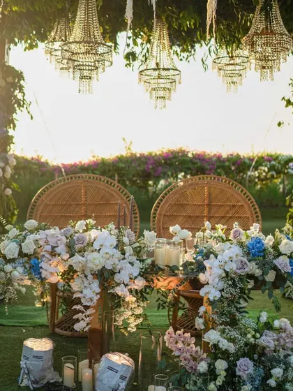 An intimate sweetheart table for the couple, framed by lush floral arrangements and hanging chandeliers. The wicker peacock chairs add a touch of bohemian elegance.