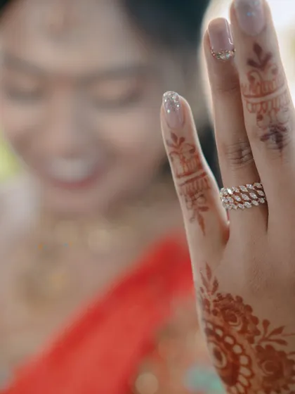 A detail shot focusing on the bride's engagement ring and the intricate mehndi on her hand, with her smiling face blurred in the background.