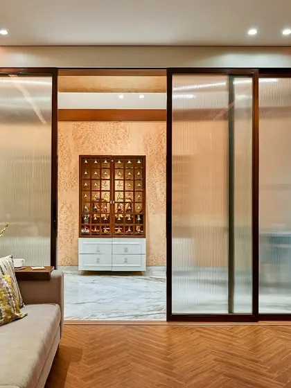 This image shows how we create separation while maintaining an open feel. The frosted glass sliding doors elegantly partition the media room from the main living area, which features a modern pooja mandir.