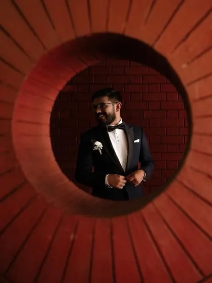 A creative portrait of a groom seen through a circular brick opening. We use architectural elements to frame our subjects in interesting ways.