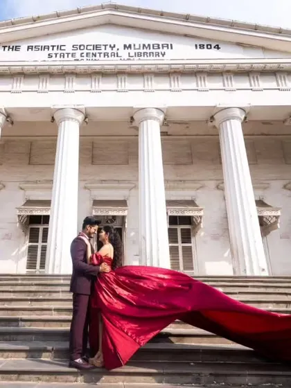 A timeless moment at Mumbai's iconic Asiatic Library. This deep maroon gown features a pleated yoke and a modern slit, offering a sophisticated and regal look for shoots in architectural settings.