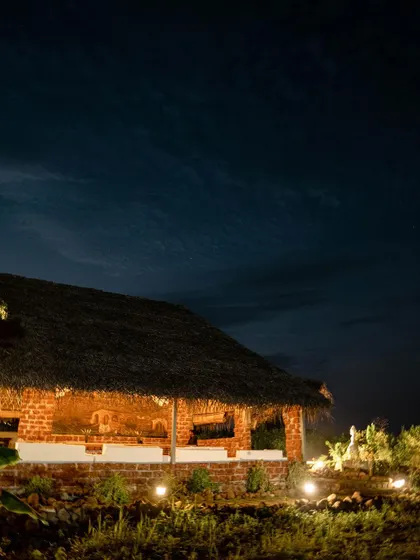 One of our charming brick and thatch huts illuminated at night. These structures add to the rustic, retreat-like feel of our Ananthagiri Hills property.
